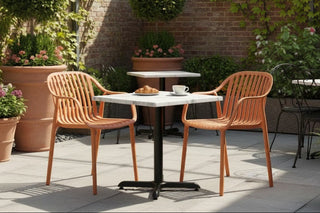 Outdoor patio with wooden chairs and tables surrounded by potted plants and a brick wall.